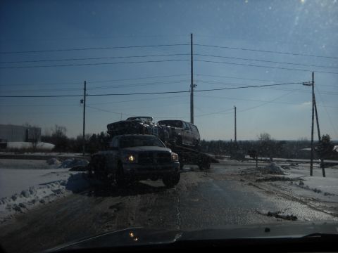 1993 Ford C-150 (Centurion Conversions) - A truck tows a car and an SUV on a trailer through a snowy landscape under a clear blue sky.