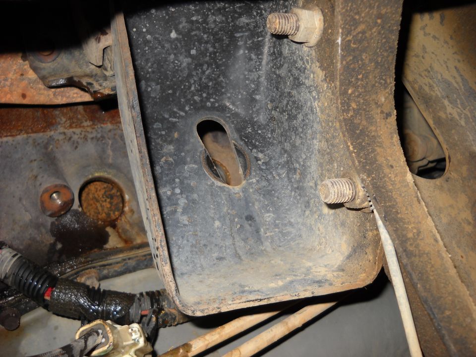 Rusty frame bracket with two bolts and a hole. Wiring harness visible below