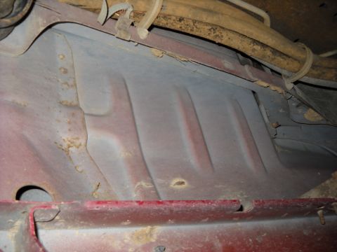 1993 Ford C-150 (Centurion Conversions) - Underbody view of a red vehicle, revealing frame rails and fuel lines, with some signs of rust.