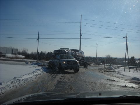 1993 Ford C-150 (Centurion Conversions) - Multiple vehicles are being transported on a trailer in a snowy environment.