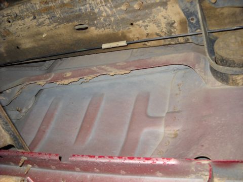 1993 Ford C-150 (Centurion Conversions) - The underside of a vehicle displays significant rust and corrosion on its frame and body panels.