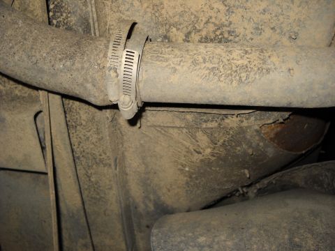 1993 Ford C-150 (Centurion Conversions) - Close-up view of an exhaust pipe held by a hose clamp, with visible rust and accumulated dirt.