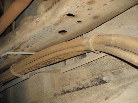 1993 Ford C-150 (Centurion Conversions) - Close-up view of the underbody chassis and fuel lines of a vehicle, showing rusted metal and dust accumulation.