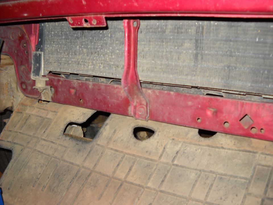 Close-up of a red vehicle's front radiator support and lower splash shield