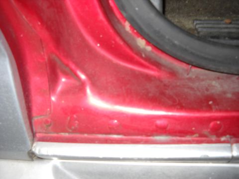 1993 Ford C-150 (Centurion Conversions) - Close-up of a damaged red vehicle door sill, showing dents and wear.
