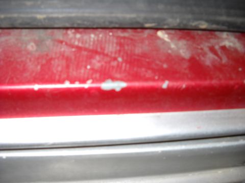 1993 Ford C-150 (Centurion Conversions) - Close-up of a red vehicle's lower body panel showing wear and tear.