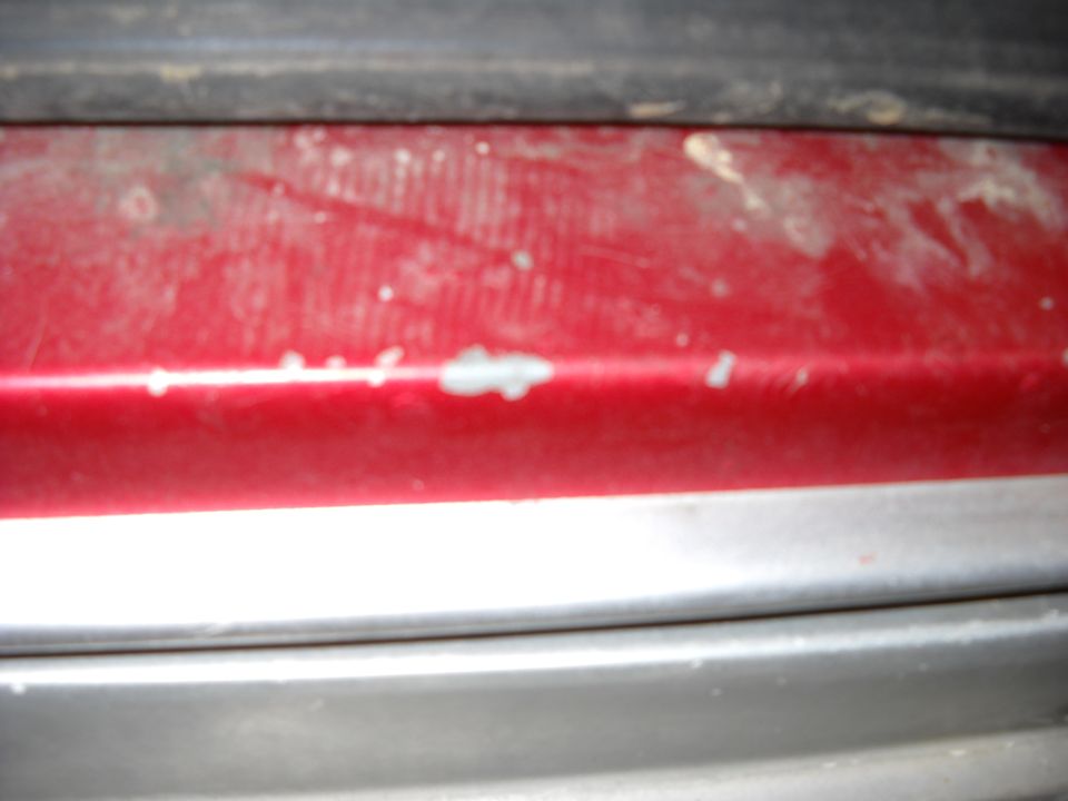 Close-up of chipped red rocker paint over silver lower panel with primer showing