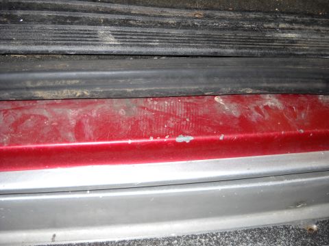 1993 Ford C-150 (Centurion Conversions) - Close-up of a red and silver lower body panel showing wear and tear.