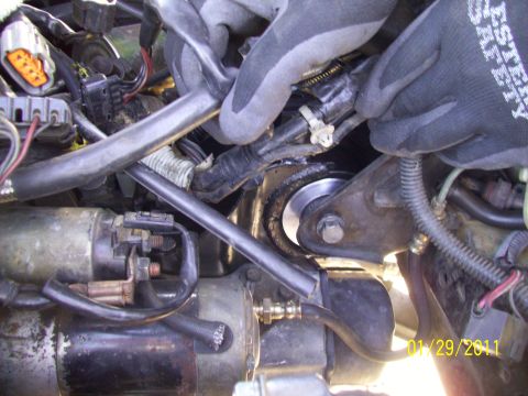 1995 Ford Probe - Mechanic's hands work on engine components, including the starter motor, in a vehicle's engine bay.