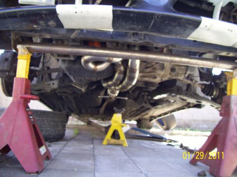1995 Ford Probe - The undercarriage of a vehicle is shown, custom exhaust headers and being supported by jack stands.