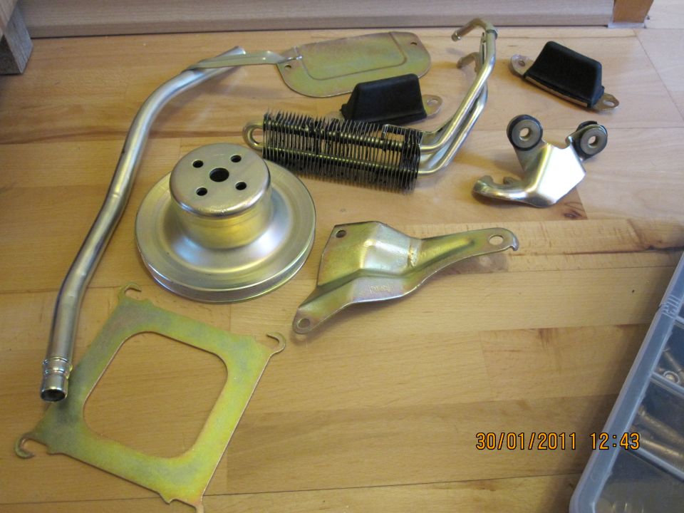 Assorted metal vehicle parts, including a pulley and a small radiator-like component, laid out on a wooden surface