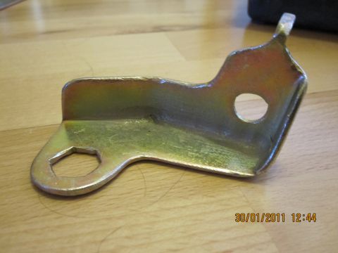 1973 Ford Ranchero - Metal bracket with hex and round holes, photographed on a wooden surface.