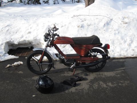 1981 Garelli Rally Sport - A red moped sits on a paved surface with snowdrifts behind it, accompanied by a helmet and gloves.