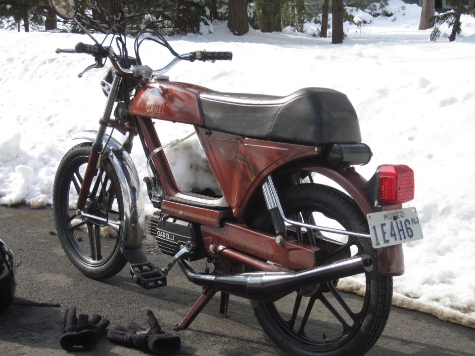 Red Garelli moped with black seat and chrome accents, parked on asphalt with snow in background