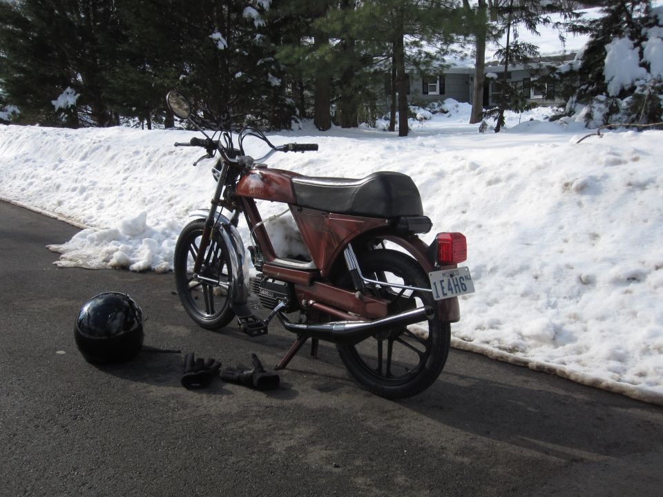 Red moped from rear, parked on asphalt with snowbanks