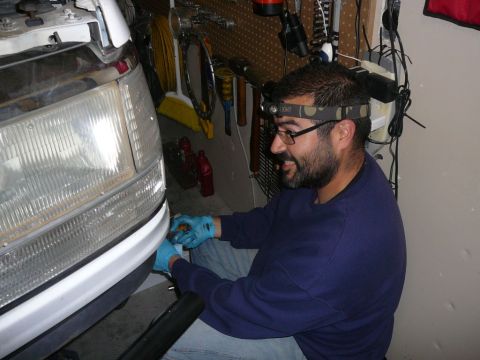1988 Ford Bronco - A man wearing a headlamp works on the front end of a white vehicle in a garage setting.