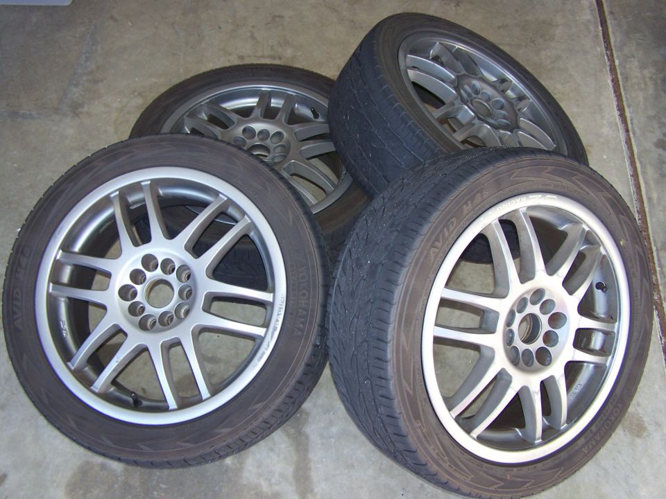 Four gunmetal split-spoke alloy wheels on Yokohama AVID tires stacked on concrete