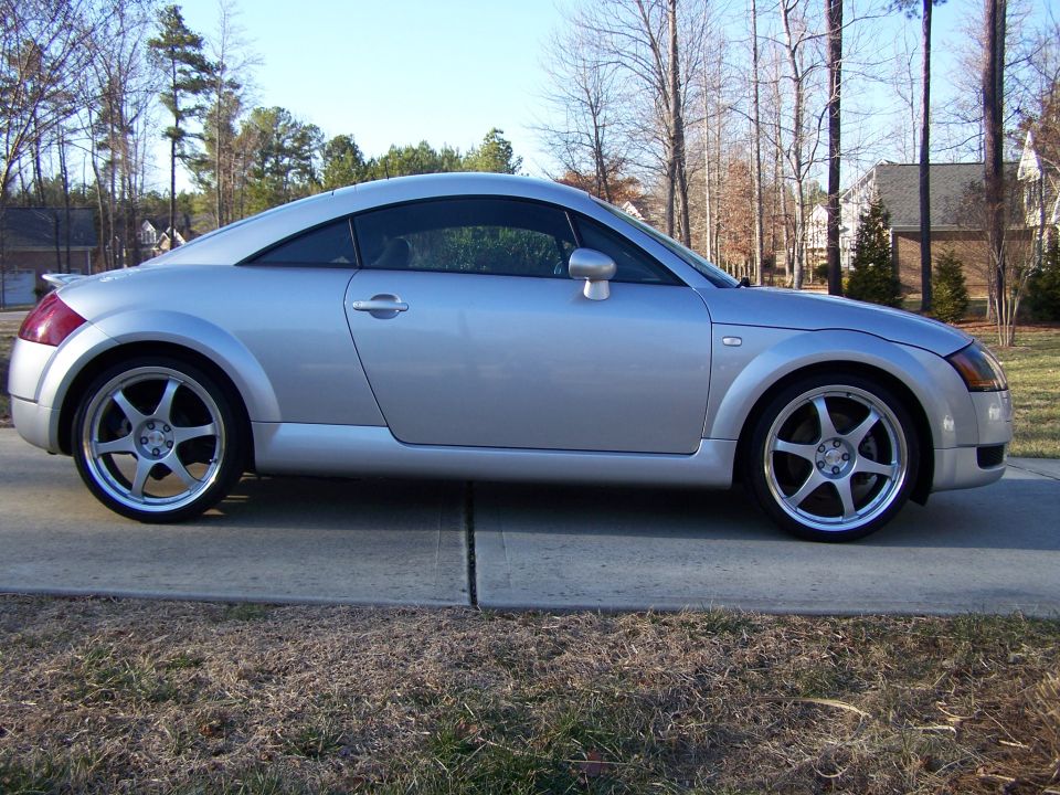 Silver Audi TT coupe side profile on driveway with six-spoke polished-lip wheels