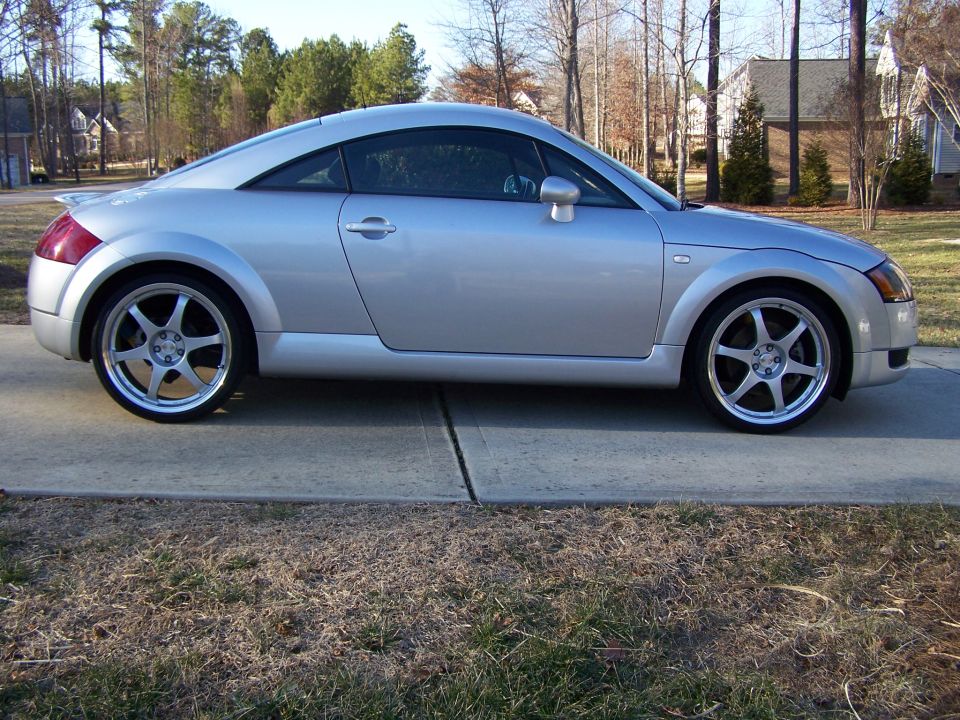 Silver Audi TT coupe side profile on driveway with aftermarket five-spoke wheels