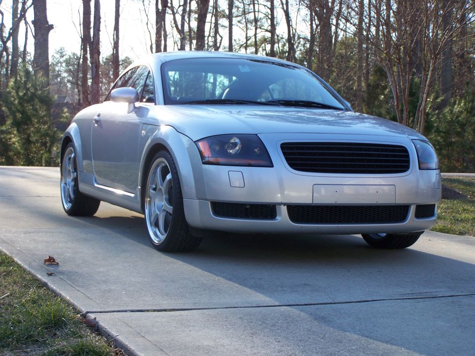 Silver Audi TT coupe front three-quarter view on driveway with polished lip wheels