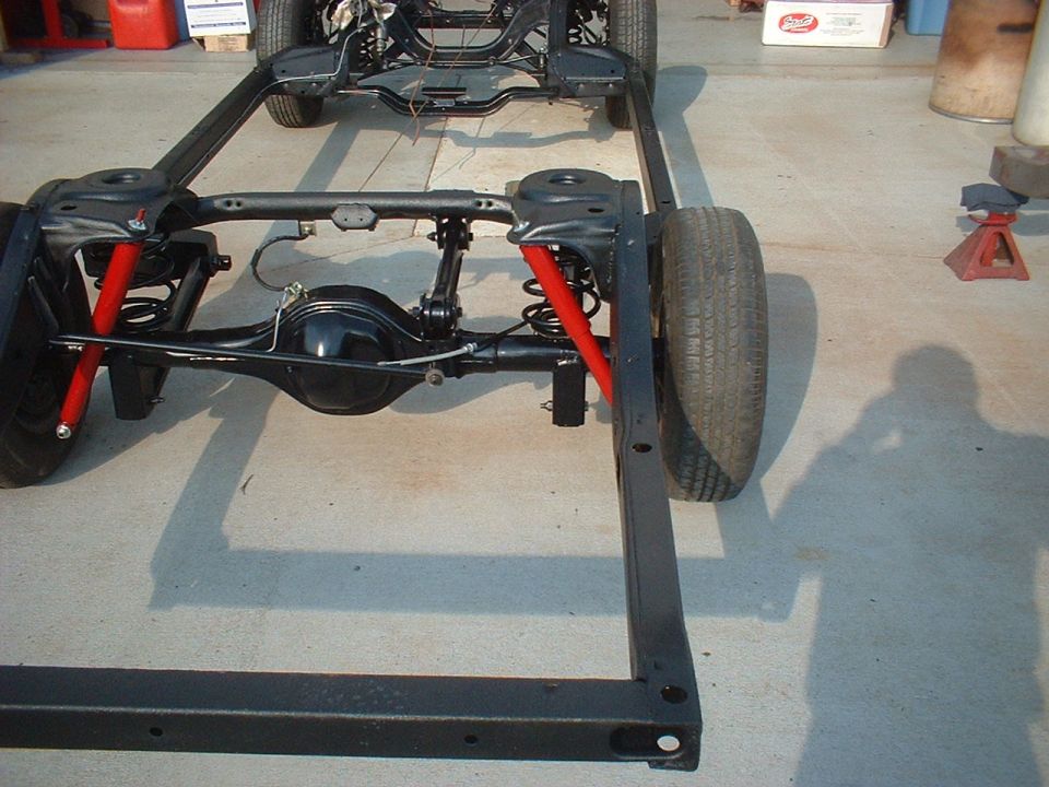 Car frame with rear suspension and one wheel visible. Red shocks are installed