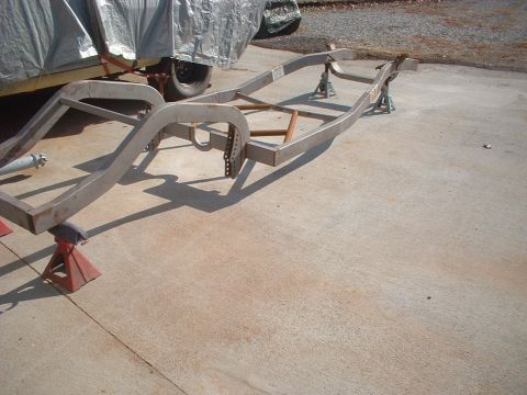 1969 Ford Torino - A bare car frame rests on jack stands, with a tarp-covered vehicle visible behind it.