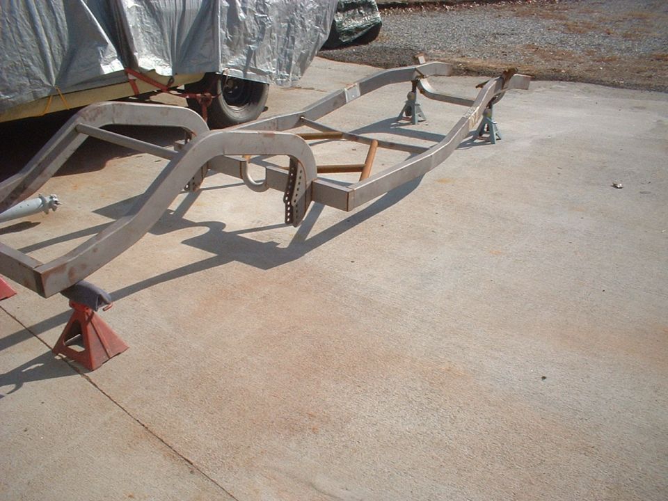 Car frame on red jack stands, partially covered vehicle in background