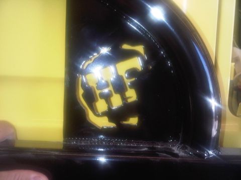 1978 Ford Bronco - A close-up of a yellow and black emblem on a vehicle's exterior, with website text visible at the bottom.