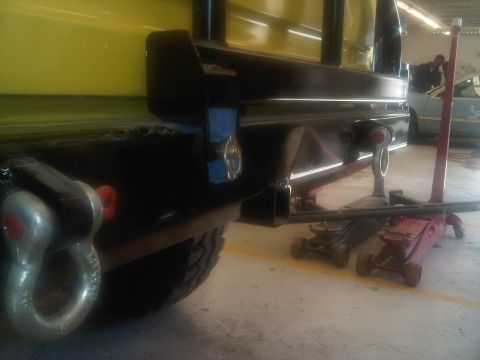 1978 Ford Bronco - A vehicle's rear bumper assembly, a large tow hitch and shackle, is shown with floor jacks supporting it.