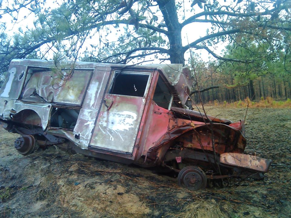 Wrecked truck body in woods, looks like it rolled and is heavily damaged