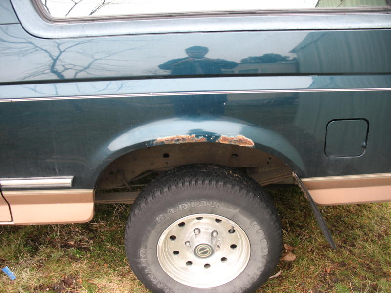 Dark green SUV rear wheel well with rust and tan trim