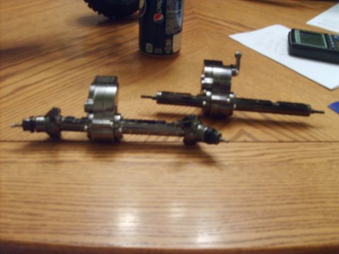 1989 Ford Bronco - Two metal axles for an RC car are laid out on a wooden table next to a can of soda and a calculator.