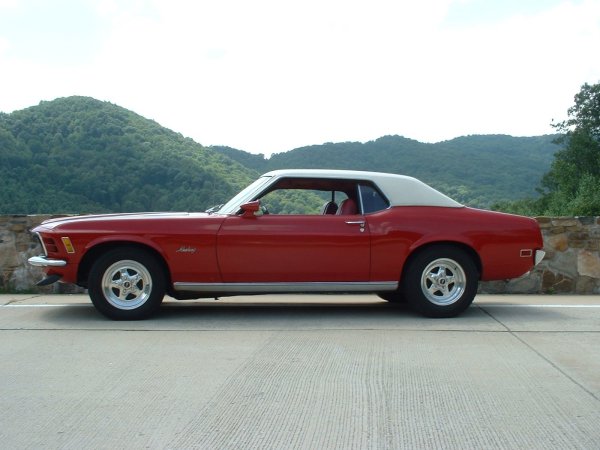 1970 Ford Mustang coupe, red with white vinyl roof, parked roadside with mountains in background