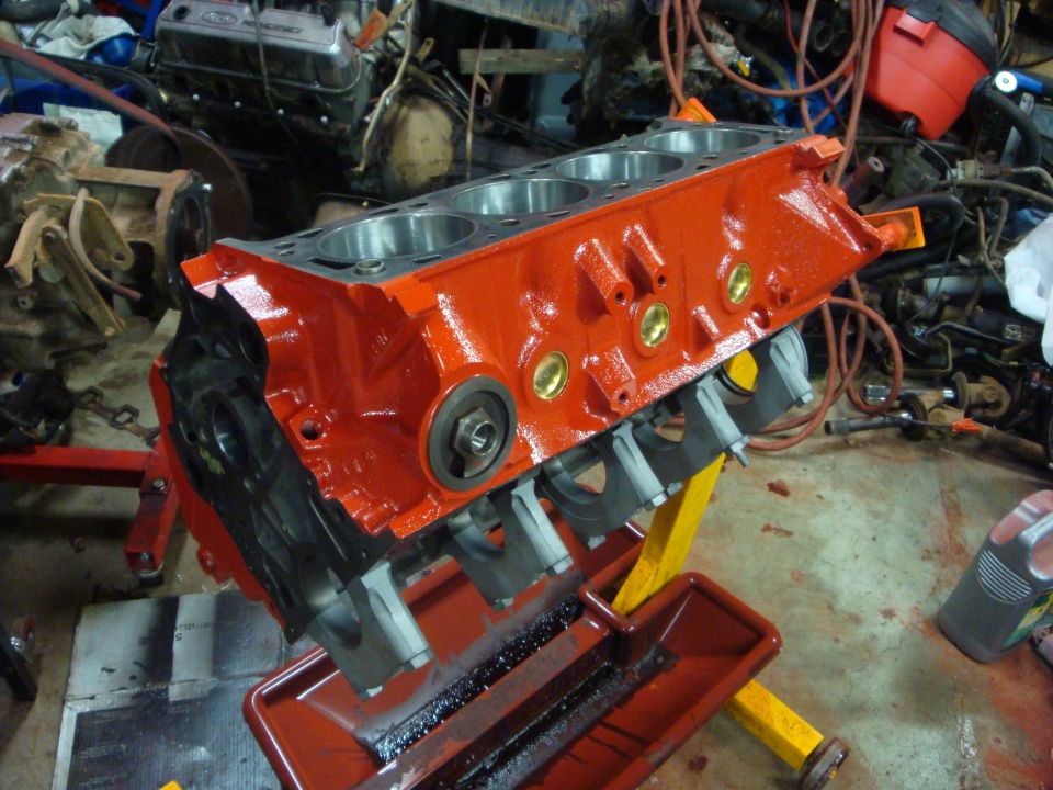 Orange-red painted V8 engine block on a stand showing main caps, brass plugs and honed bores