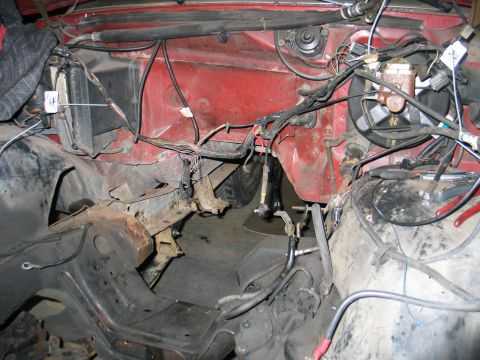 1984 Ford Bronco - Empty engine bay of a red truck with the engine pulled, showing bare red inner fenders and firewall, hanging wiring harnesses with tagged c…