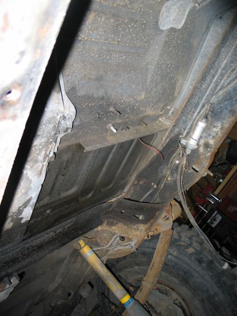 1984 Ford Bronco - The underside of a vehicle shows suspension parts and signs of wear and tear.