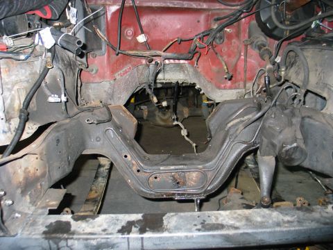 1984 Ford Bronco - The engine bay and frame of a vehicle are exposed, revealing the transmission tunnel and extensive wiring.