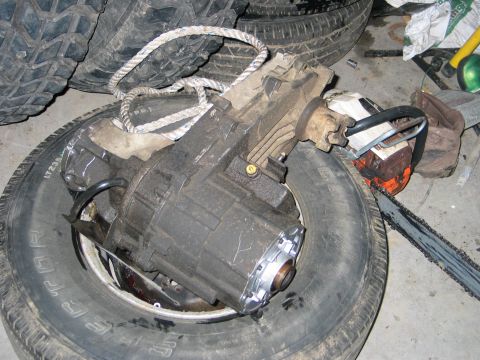 1984 Ford Bronco - A transfer case rests on a tire, with a chainsaw visible to the right.