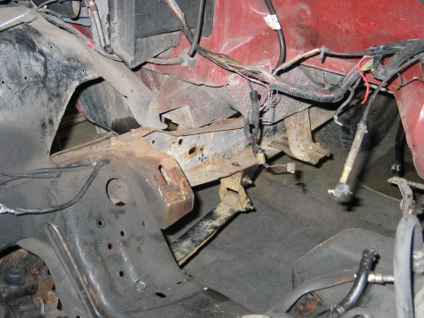 1984 Ford Bronco - Close-up view of the engine bay and frame of a red vehicle, showing signs of rust and exposed wiring.