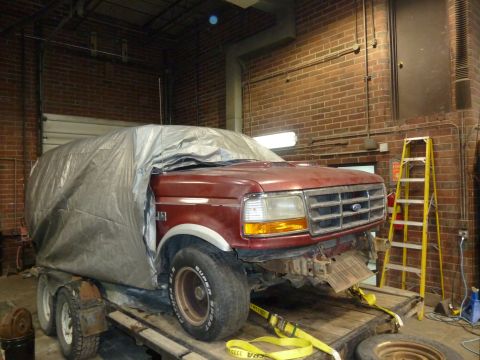1993 Ford C-150 (Centurion Conversions) - A red pickup truck is parked on a trailer inside a garage, partially covered by a tarp.
