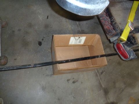 1993 Ford C-150 (Centurion Conversions) - A cardboard box sits on a concrete floor next to a trailer's taillight and a yellow strap.