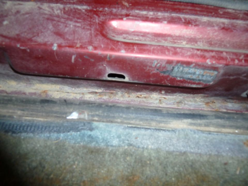 Red interior door sill with visible rust and dirt. A small black hole is present