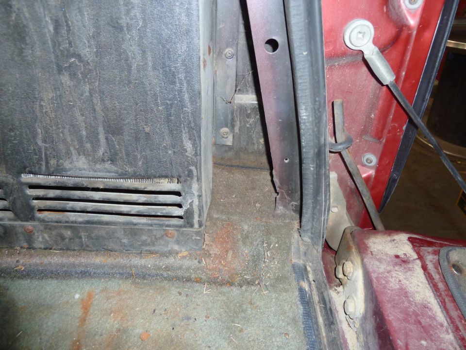 Close-up of a vehicle's interior floor, showing carpet, a vent, and the door jamb area
