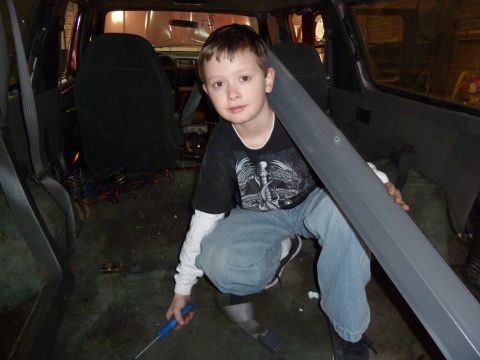 1993 Ford C-150 (Centurion Conversions) - A young boy kneels in the interior of a vehicle, holding a piece of trim and a screwdriver.