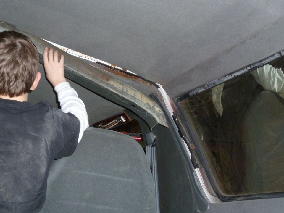 Kid's hand touching the roof trim inside a vehicle, showing rust and wear