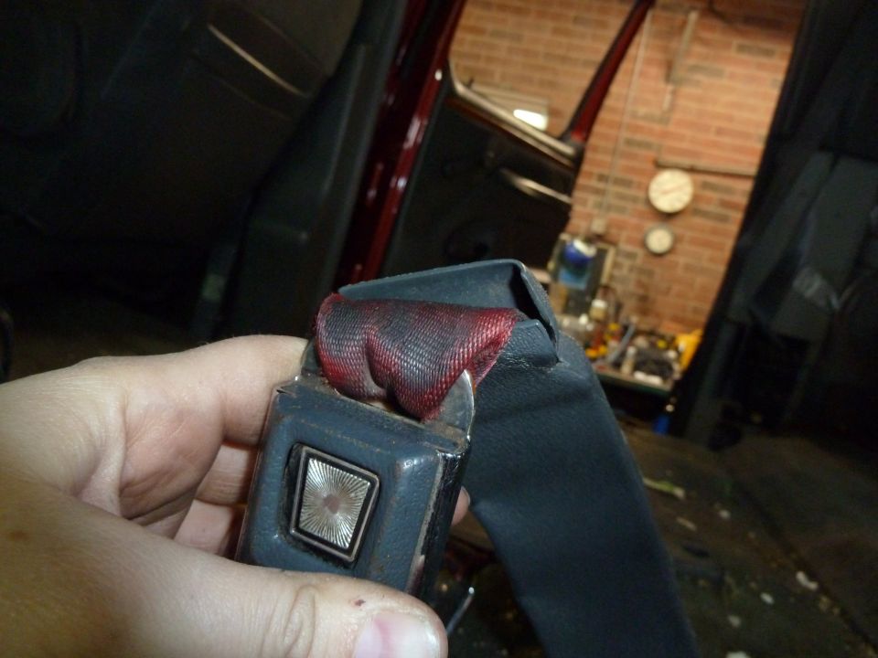 Hand holding a seatbelt buckle with a red and black patterned strap