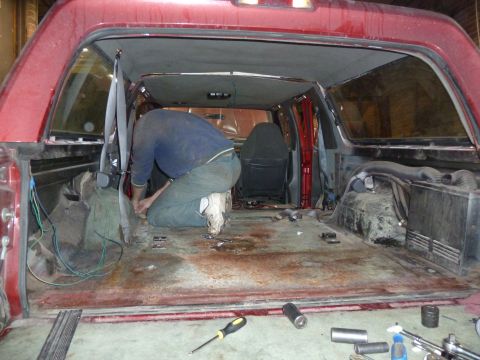 1993 Ford C-150 (Centurion Conversions) - The interior of a red SUV is shown with the rear seats removed and a person working on the wiring and floor.