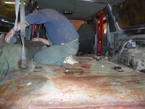 1993 Ford C-150 (Centurion Conversions) - Interior of a van undergoing work, with a person attending to wiring and the floor stripped bare.