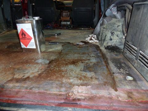 1993 Ford C-150 (Centurion Conversions) - The interior of a vehicle shows a rusty floor with a container of flammable liquid and some tools.
