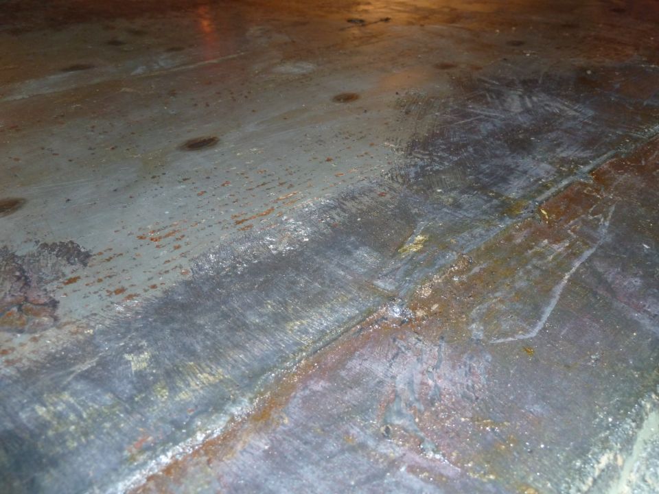 Ground and rust-treated bare steel floor pan with spot welds and sanding marks